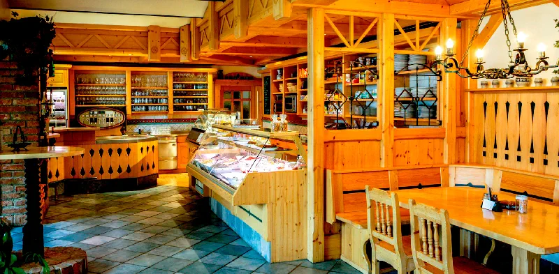 Ein gemütliches Restaurant-Interieur im Weinviertel-Charme mit Holzmöbeln und Regalen, einer Vitrine voller Speisen und warmer Beleuchtung. Tische und Stühle stehen auf einem gefliesten Boden und vermitteln die einladende Atmosphäre des Heurigen GILG.